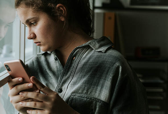 Teen looking out of window holding phone in hands